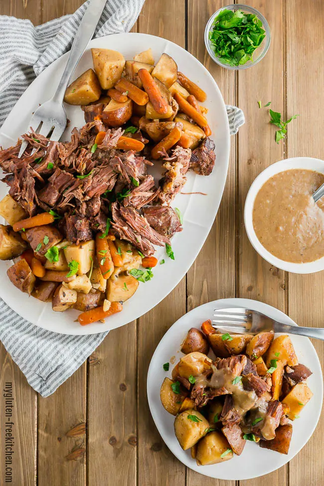 Gluten-free Slow Cooker Pot Roast on a platter with a bowl of gravy beside it