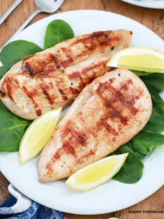 Grilled Lemon chicken breasts on plate with spinach and lemon wedges
