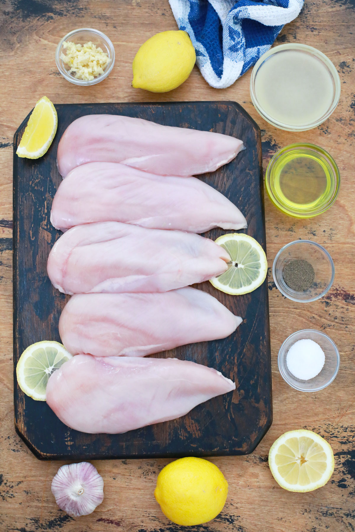 Ingredients for gluten-free chicken marinade including plate with raw chicken, lemon wedges and small bowls with oil salt and pepper