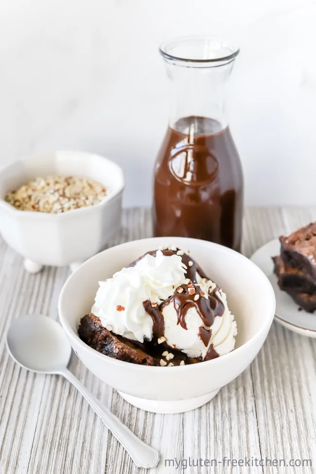 Gluten-free Hot Fudge Sundae in bowl with bowl of nuts and bottle of hot fudge