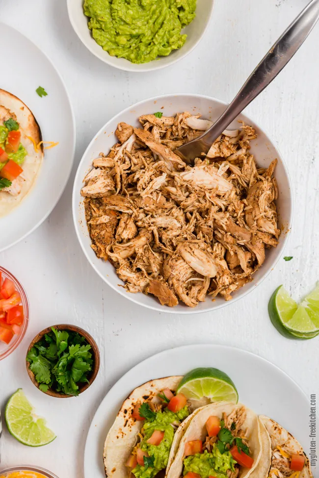 Gluten-free Shredded Chicken in bowl with taco toppings scattered around it