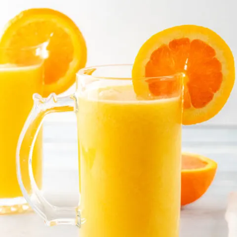 Two glasses of orange julius with orange slices scattered