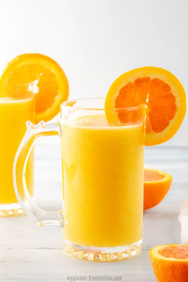 Two glasses of orange julius with orange slices scattered