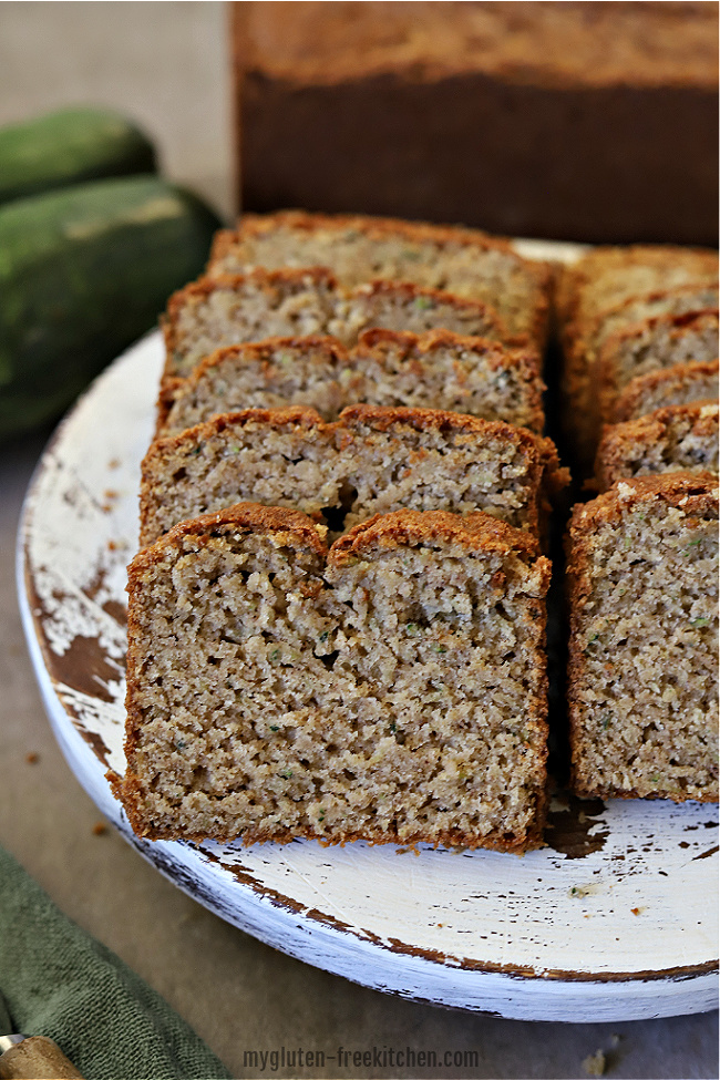 Sliced gluten-free zucchini bread on a white platter with zucchini in background