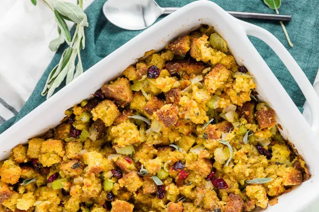 Cornbread Stuffing in white pan with sage and a spoon beside it