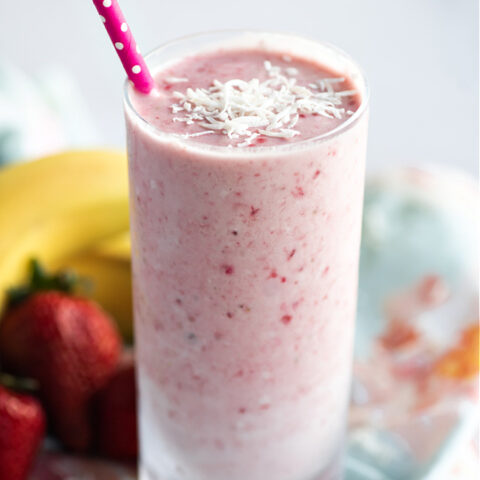 dairy-free strawberry banana coconut smoothie in glass with fresh banana and strawberries behind it on a colored towel