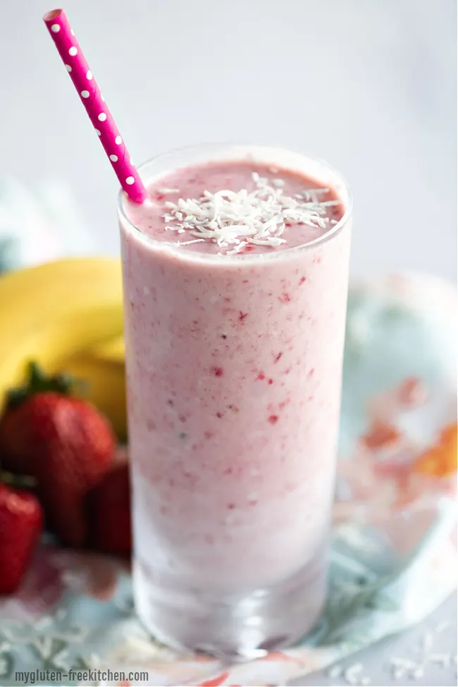 dairy-free strawberry banana coconut smoothie in glass with fresh banana and strawberries behind it on a colored towel 