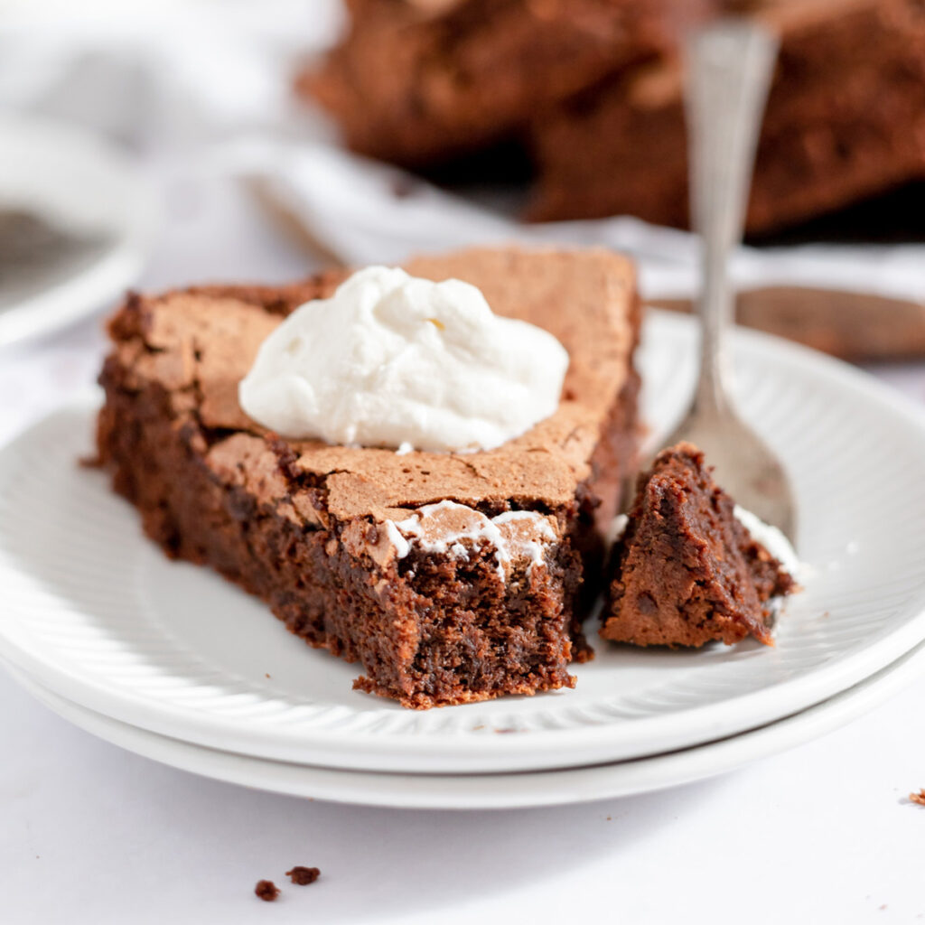 closeup image of brown slice of flourless chocolate cake with bite on fork on two small white plates