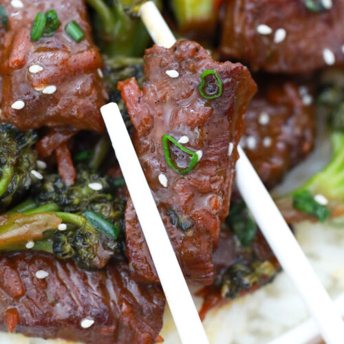 closeup image of white chopsticks grasping a piece of stir fried browned beef in gluten free beef and broccoli with broccoli nearby on white rice