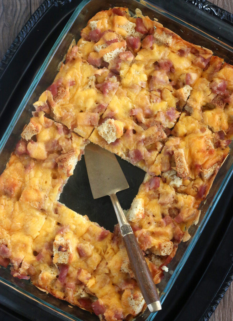 overhead image of rectangular dish with light brown chunks of bread, yellow cheese, and pink ham pieces with center piece taken